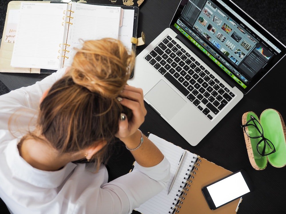 A woman sat at laptop with head in hands

